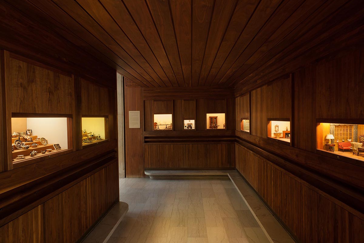 A dimly lit, wood-paneled room with small lit up boxes featuring miniature furnished rooms