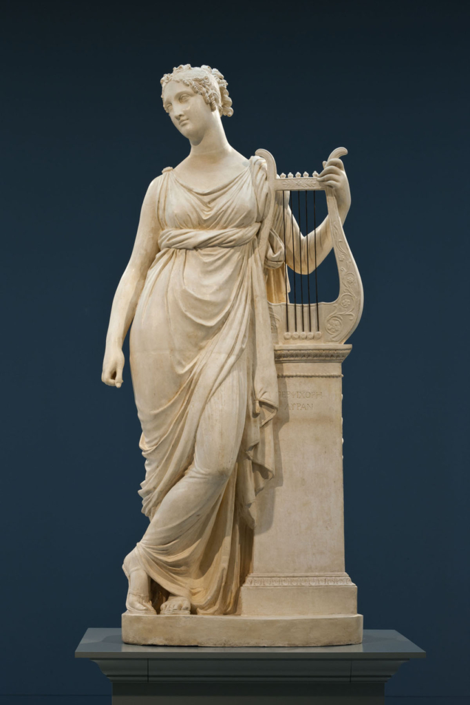 White plaster statue of a person in classical Greek dress leaning against a pedestal with one hand grasping a lyre