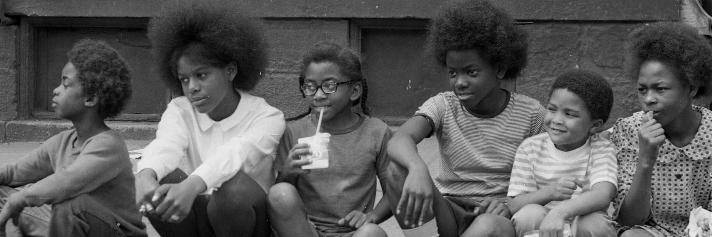 Black and white photograph depicting children seated on a curb.