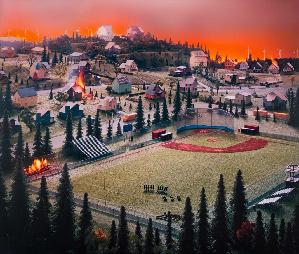 Inkjet print of a landscape with orange sky and baseball field in the foreground surrounded by a neighborhood of houses with some on fire.