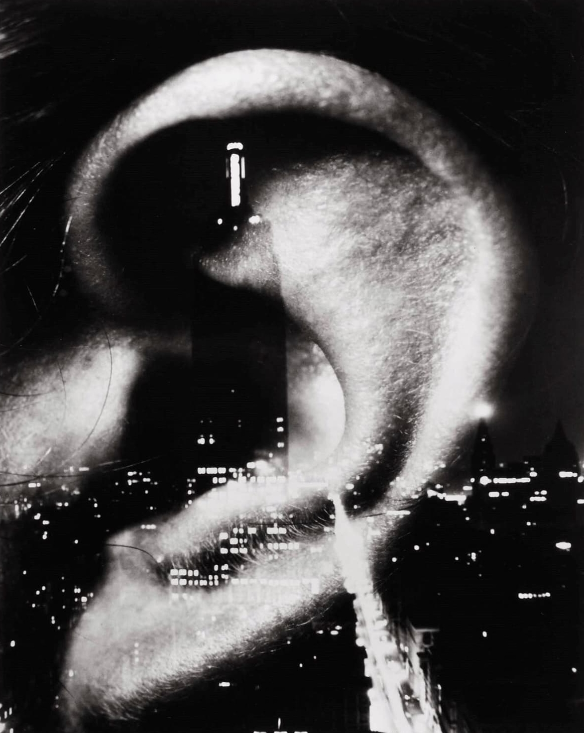 A picture of a city at night-time with a large skyscraper in the foreground. A photo of a person’s ear is layered over the city image. 