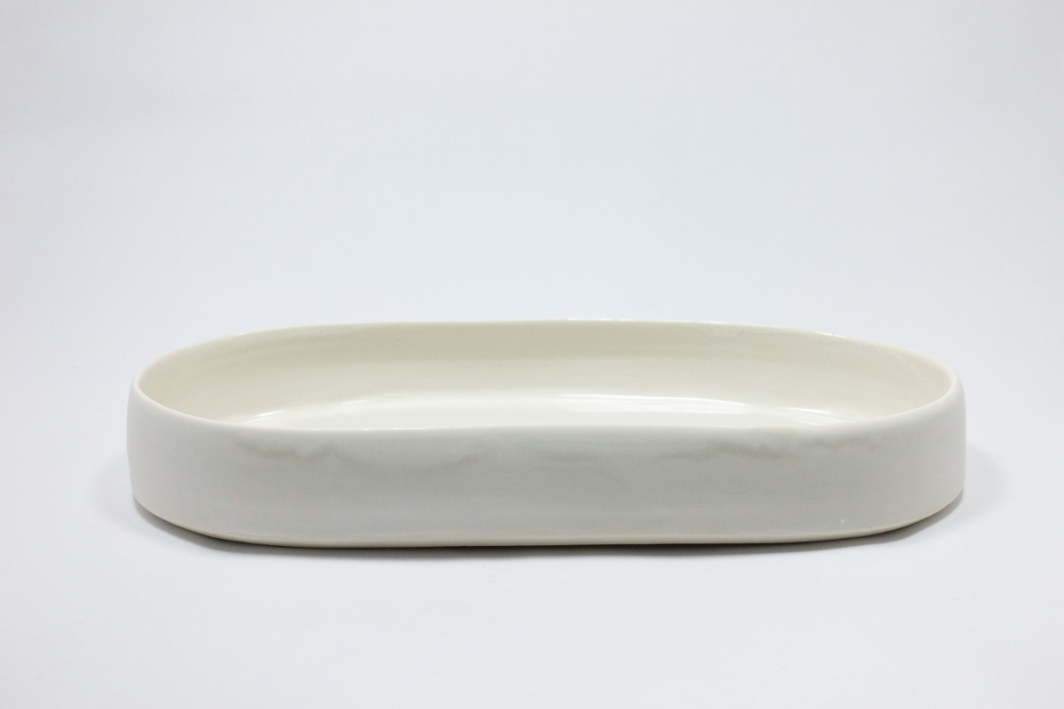 Product shot of shallow, round, light colored earth wear.