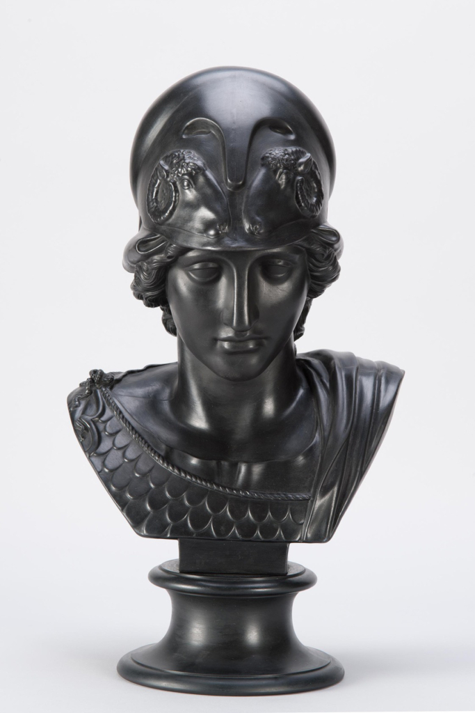 A bust of a woman wearing a warrior helmet. Cast in black stone.