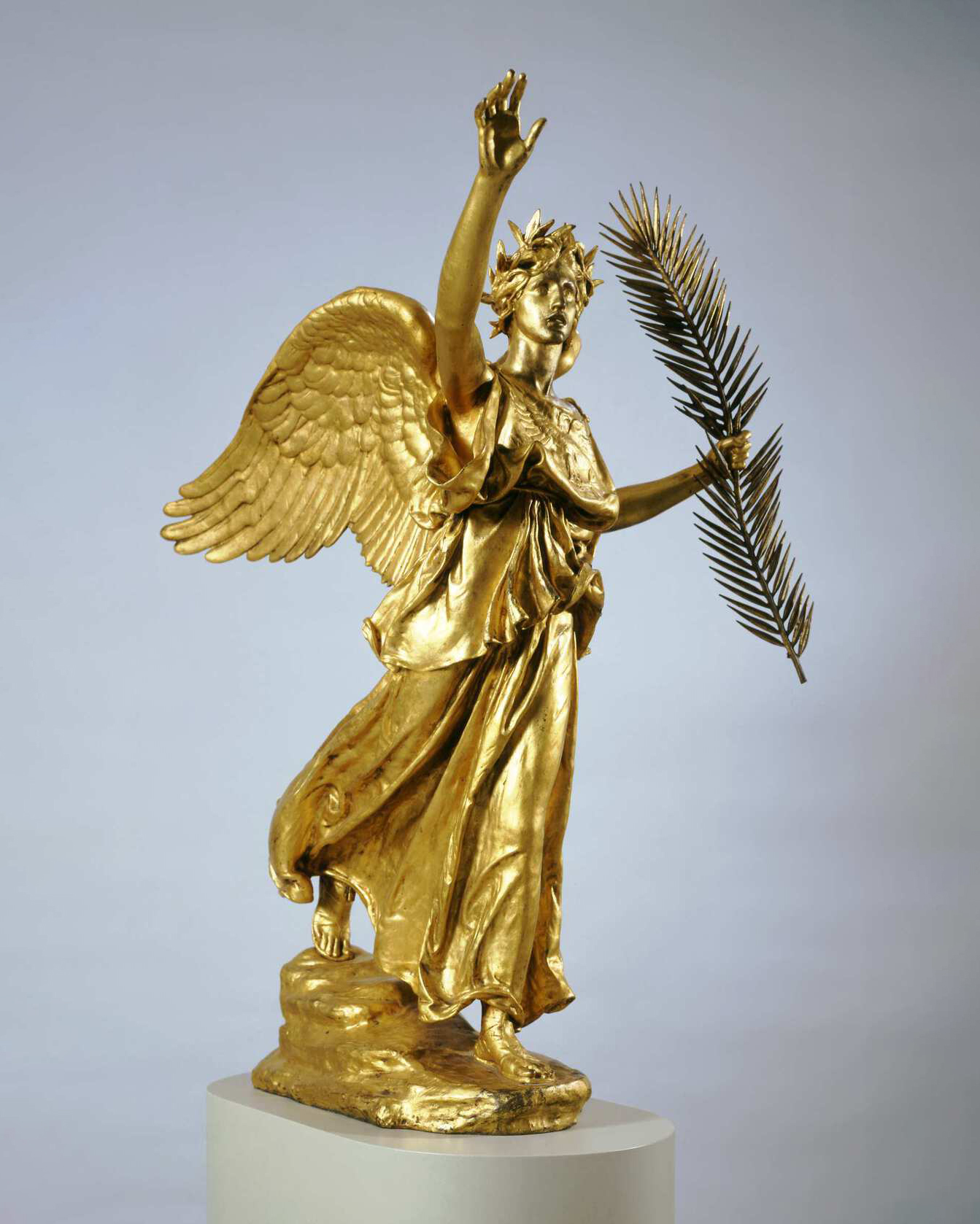 A bronze sculpture of an angel holding a palm frond in its left hand and raising its right towards the sky.
