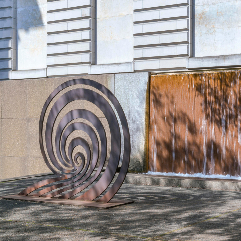 A metal sculpture in the shape of spiral sits in a courtyard.