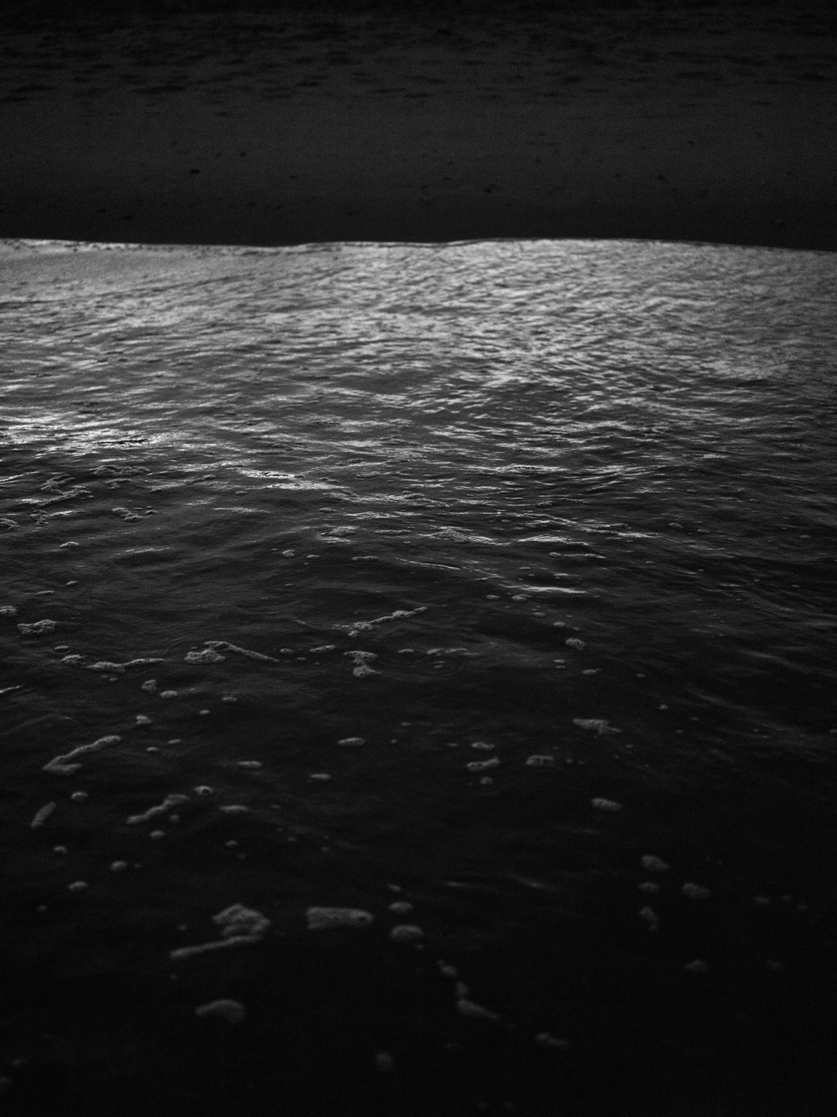 a black and white photo of water rushing to shore.