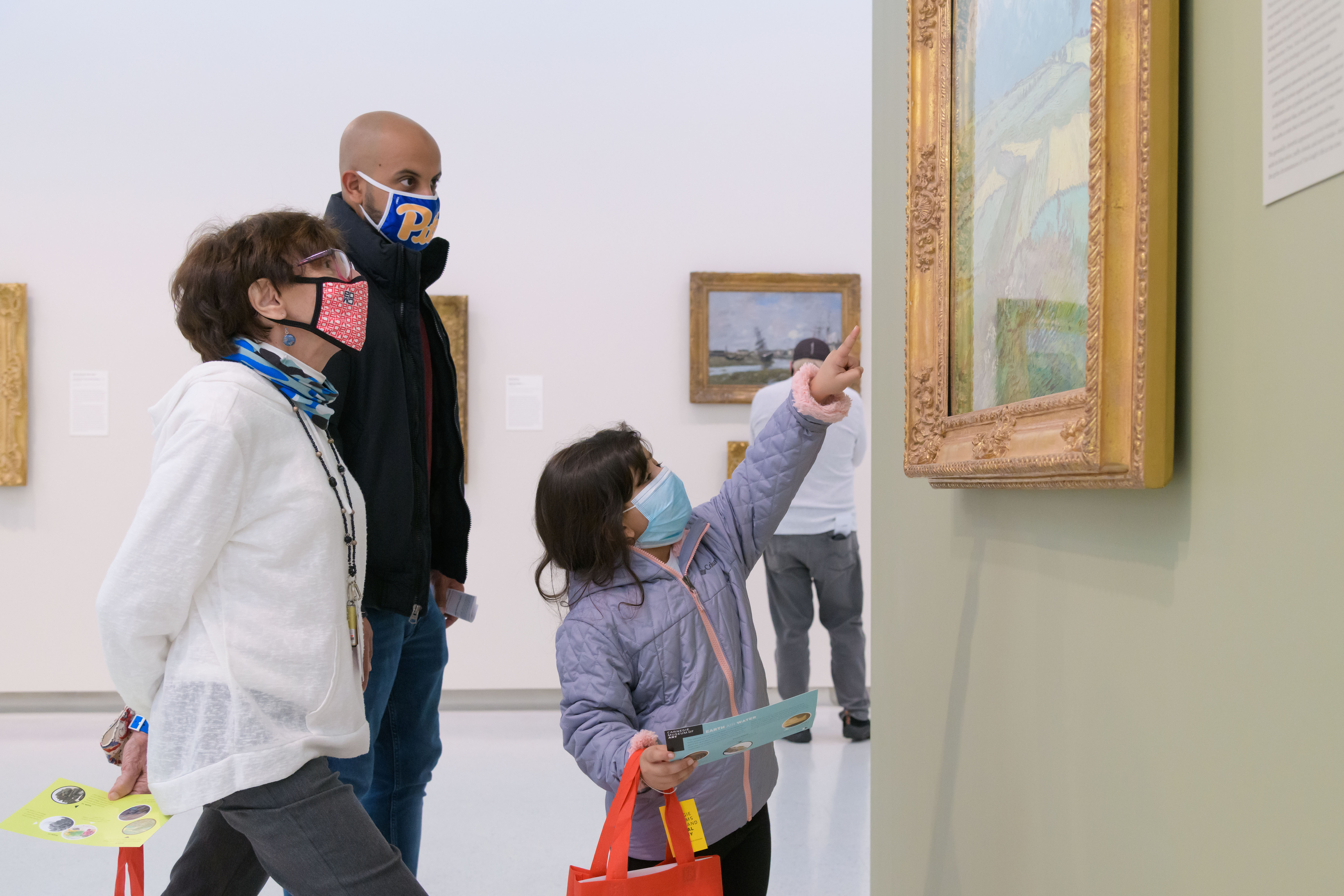 A family and a docent pay close attention to a painting.