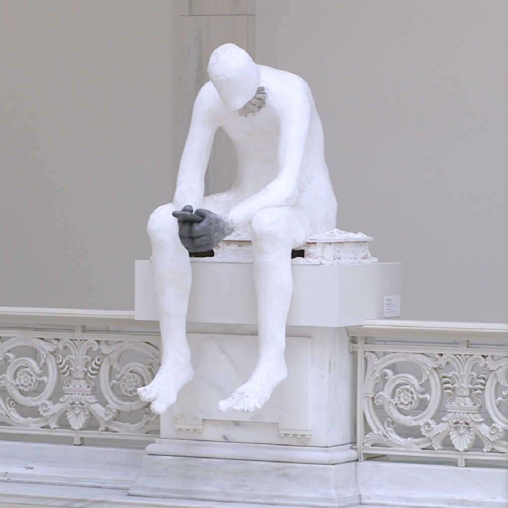 A white plaster sculpture of a man sitting over hunched over a phone