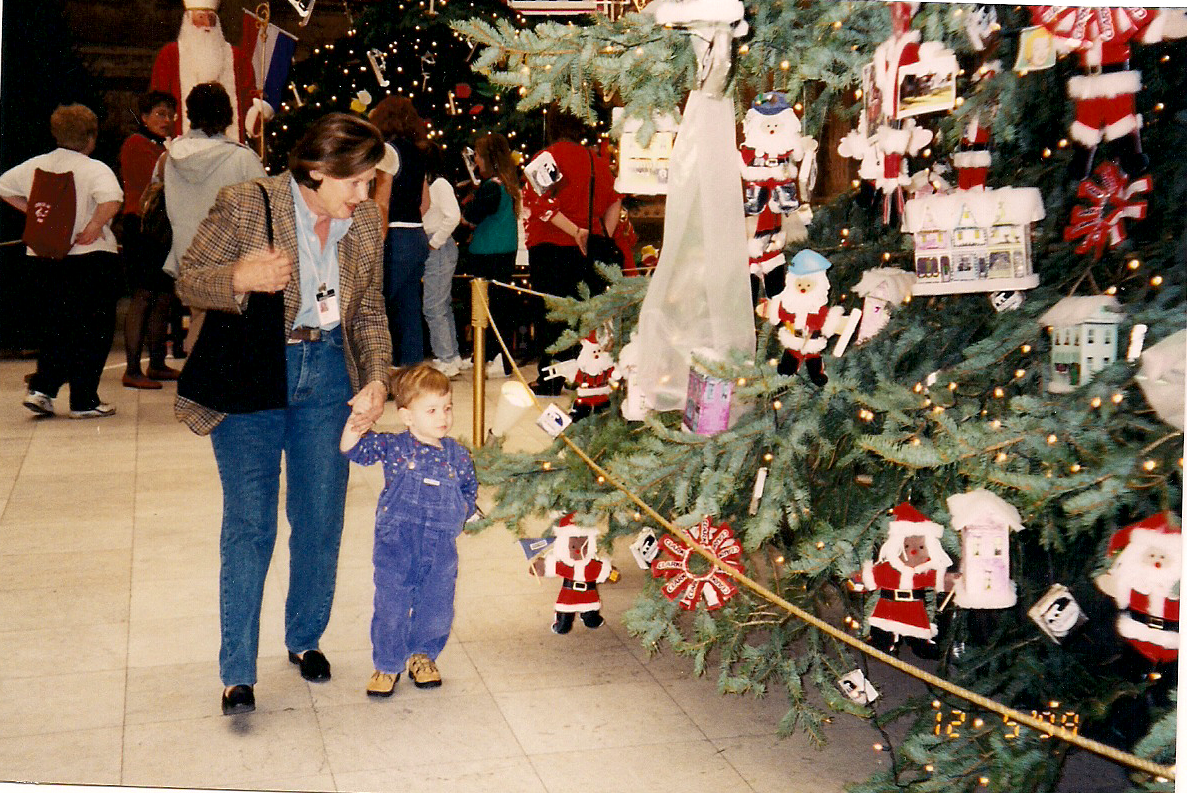 A mother and child walk by Christmas trees.