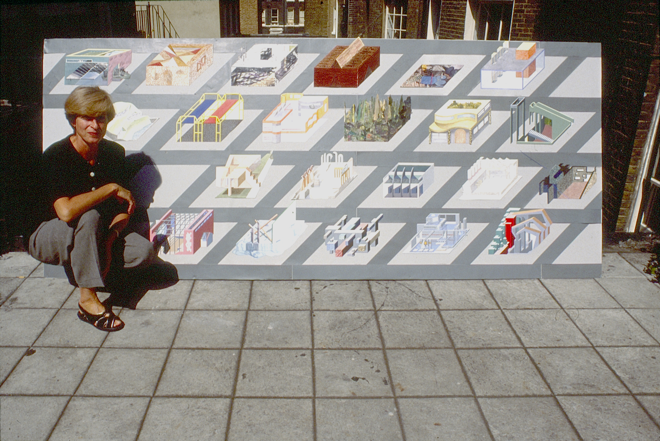 A picture of a woman kneeling in front of a board depicting different architectural plans.
