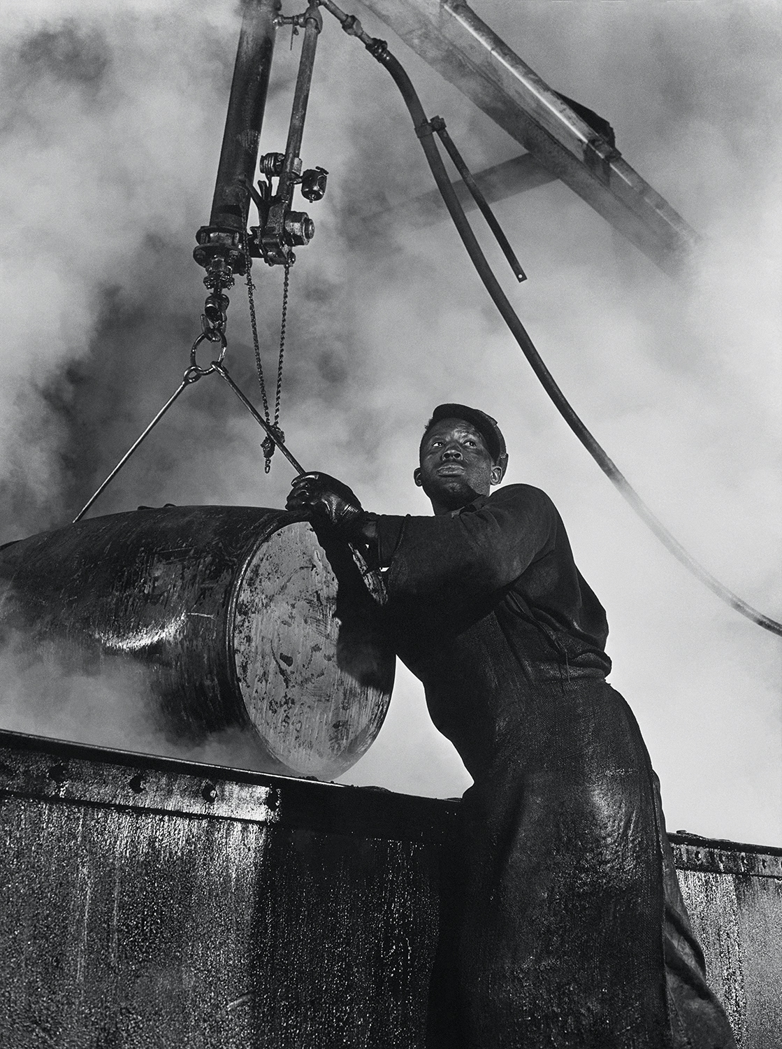 The cooper’s room where the large drums and containers are reconditioned. Here a workman lifts a drum from a boiling lye solution which has cleaned from it grease and dust particles photo by Gordon Parks