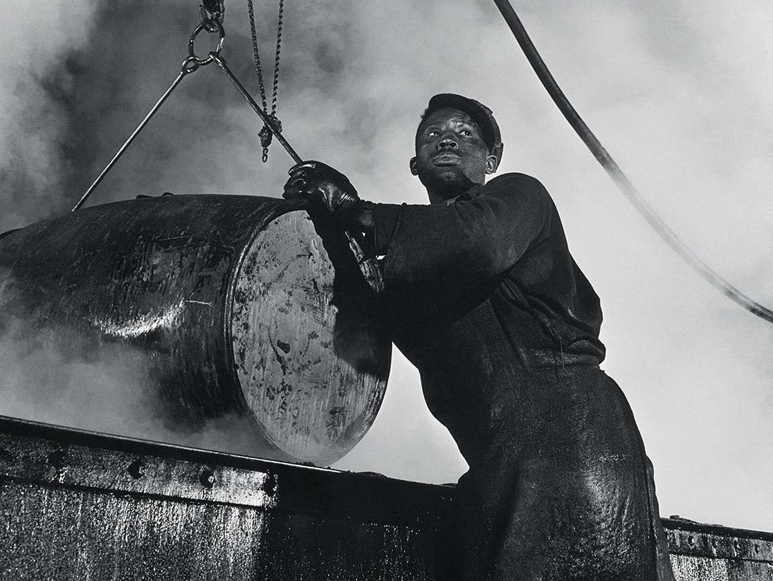 The cooper’s room where the large drums and containers are reconditioned. Here a workman lifts a drum from a boiling lye solution which has cleaned from it grease and dust particles: photos by Gordon Parks
