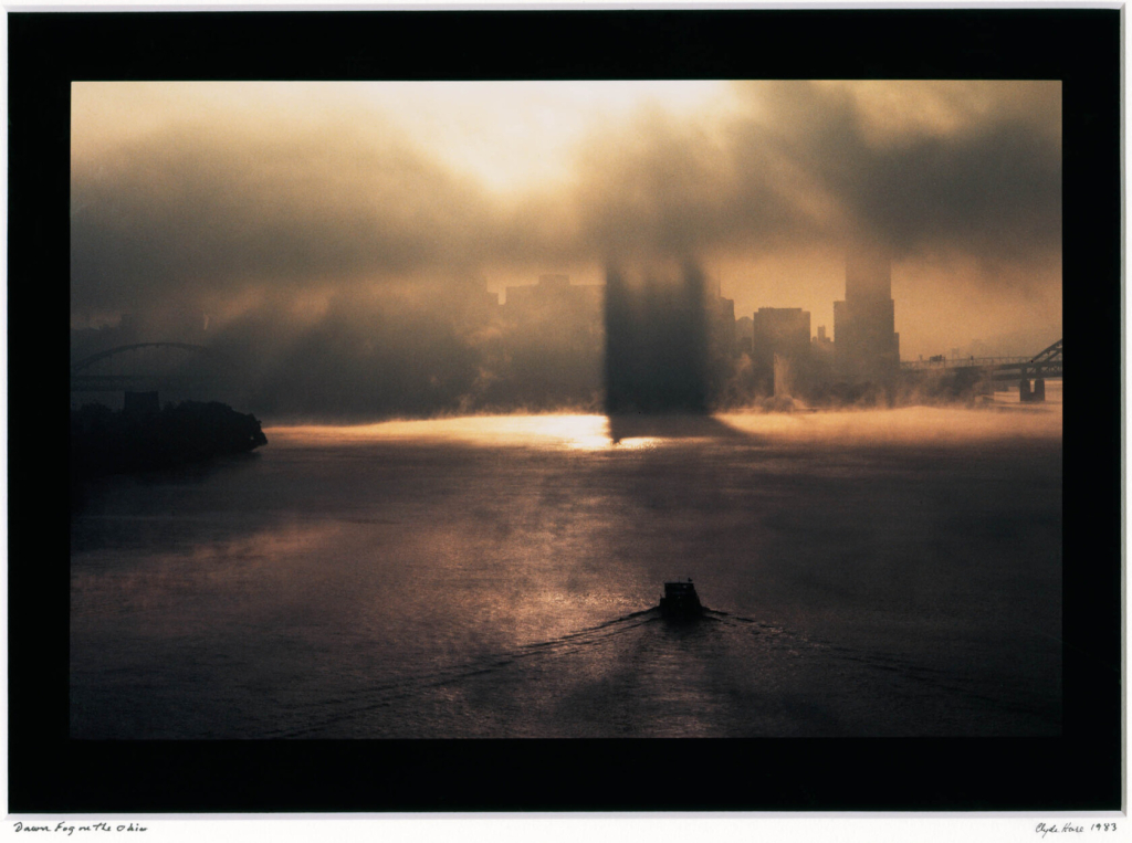 a photo of a foggy sunrise over a river with a city sky-scape looming in the distance.