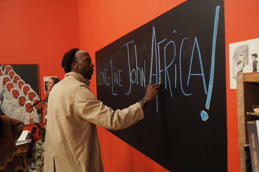 A man writes on a chalkboard: Long Live John Africa