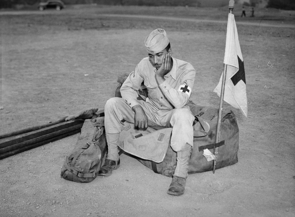 Medic soldier with cross arm band and flag, seated on duffel bag, c. 1930-1950, Carnegie Museum of Art, Heinz Family Fund by Charles Teenie Harris