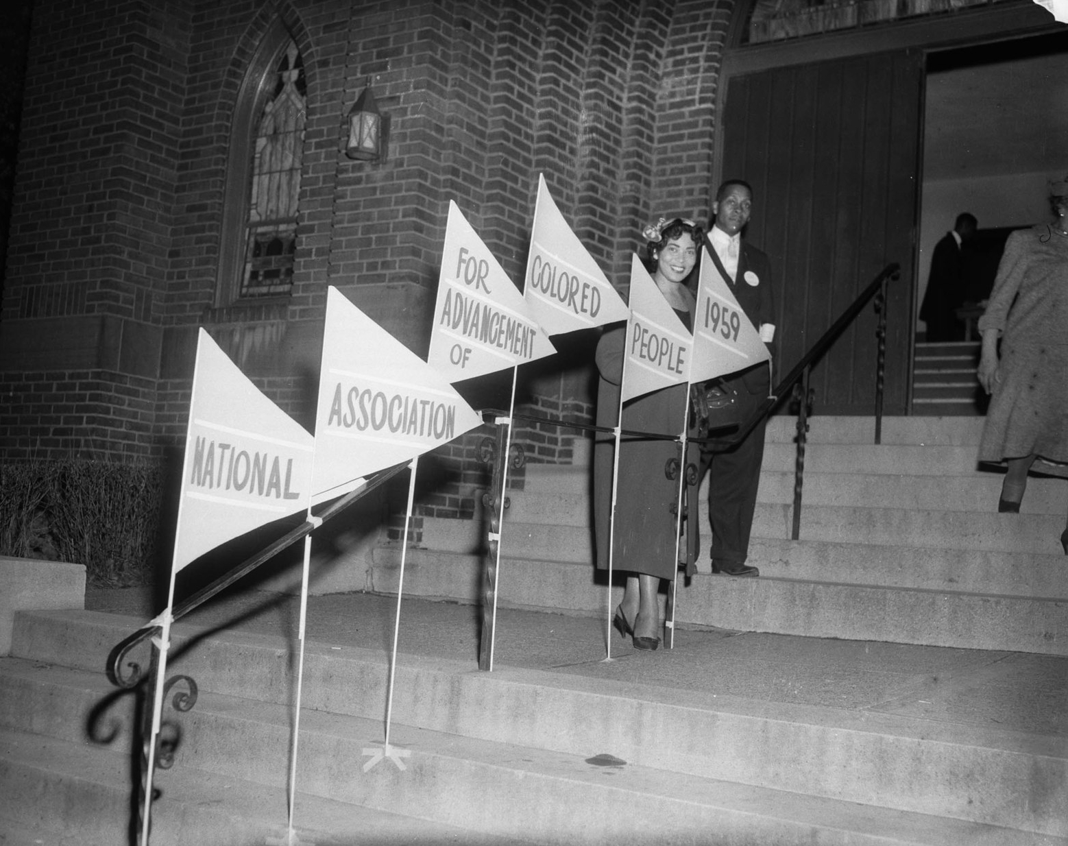 People standing on stairs leading into a church, with banner signs that read "National Organization for the Advancement of Colored People"