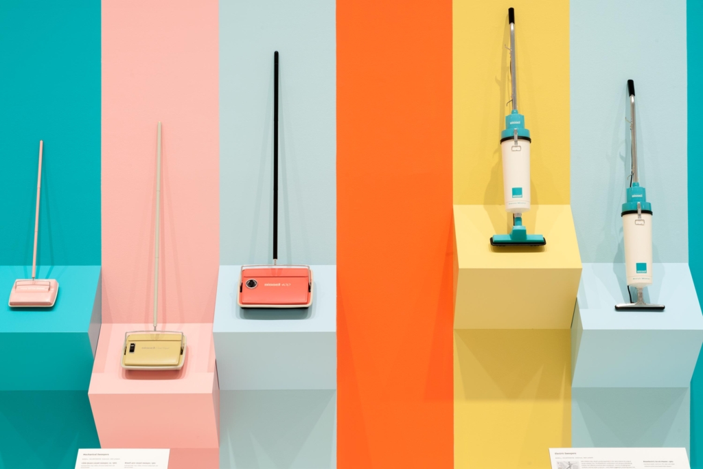 A pastel display of vacuum cleaners resting against a wall