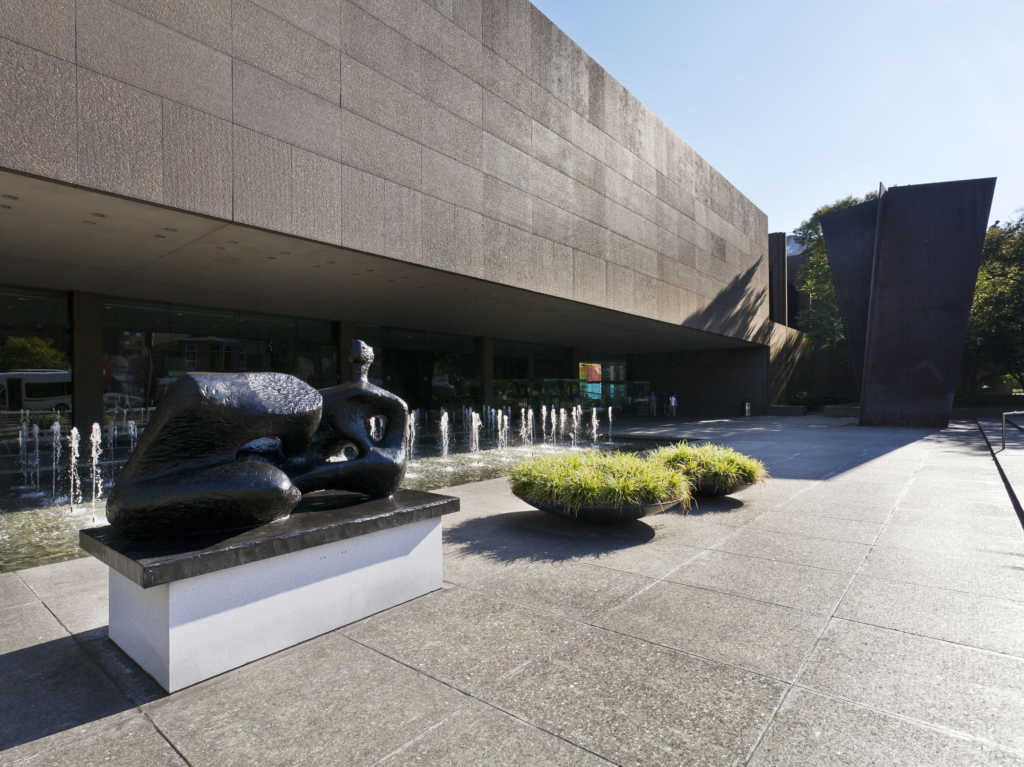 a plaza with two sculptures outside of a building underneath a cloudless sky.