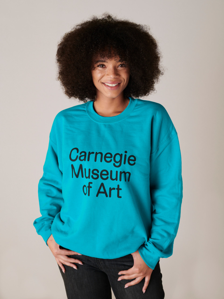 Model wearing a turquoise crewneck with the words Carnegie Museum of Art on the front