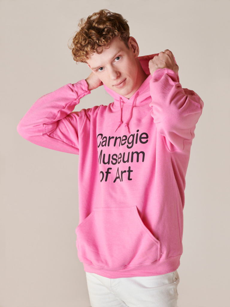 Model wearing a pink hoodie with the words Carnegie Museum of Art on the front