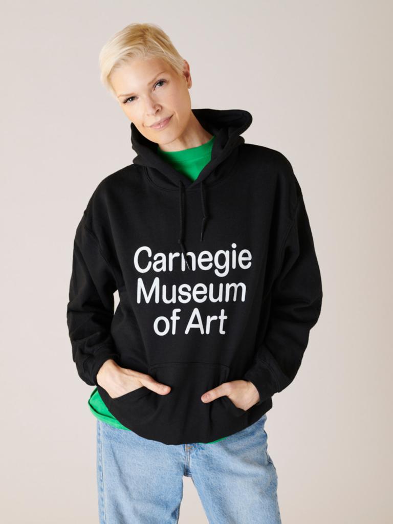 Model wearing a black hoodie with the words Carnegie Museum of Art on the front