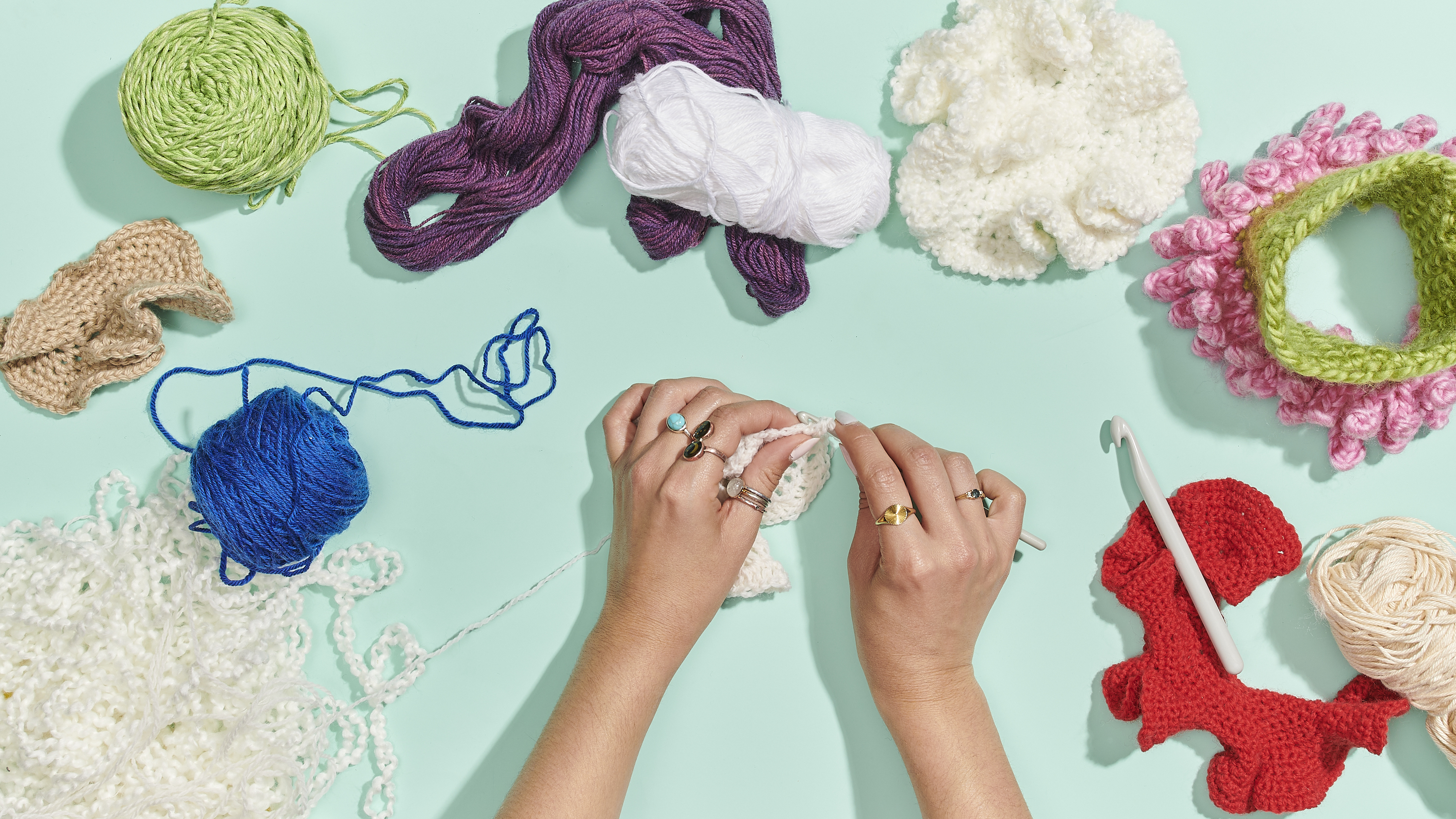 a hand that is crocheting surrounded by yarn against a bright table