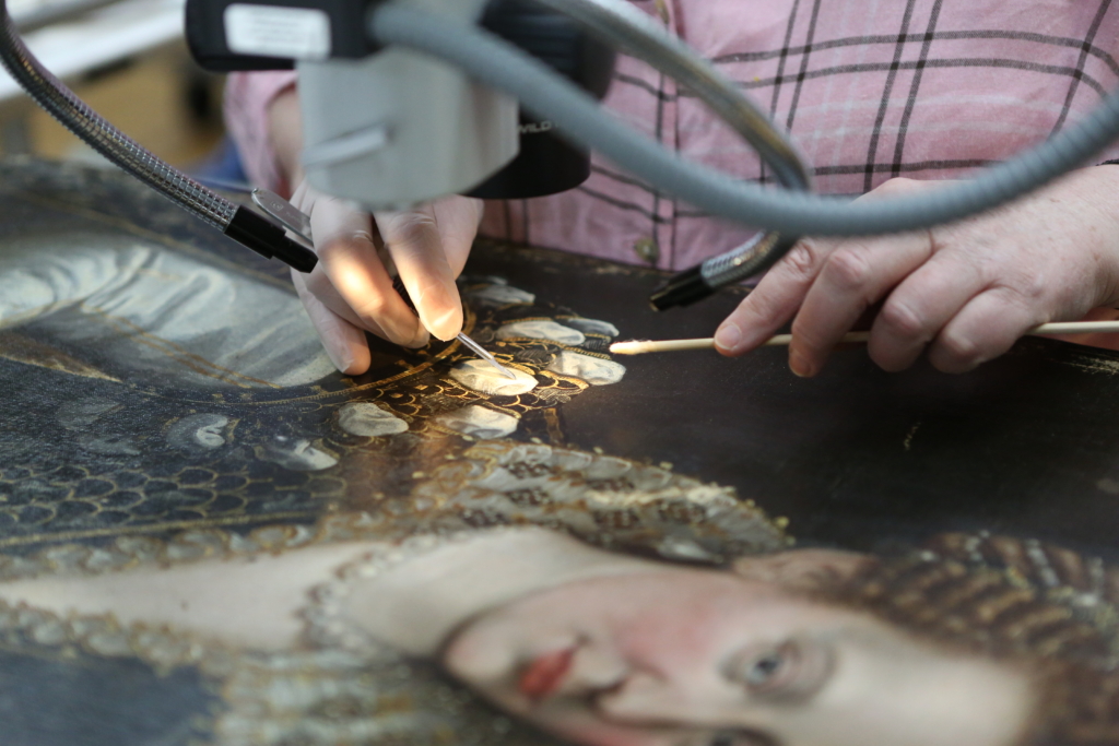 Faked, Forgotten, Found Four Renaissance Paintings Investigated Exhibition Image featuring an art conservator cleaning a portrait painting delicately with precise tools