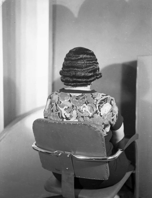 Charles Teenie Harris Woman in floral dress seated in armchair seen from behind, modeling hairstyle, in Harris Studio