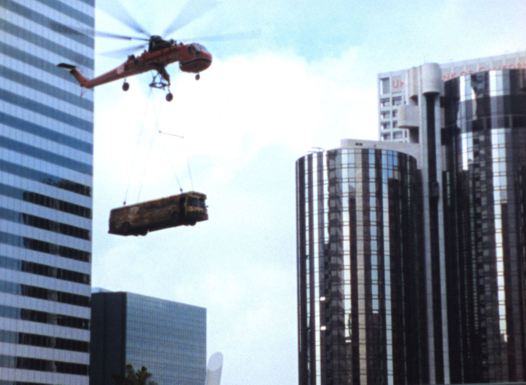 a schoolbus hanging from a special transport helicopter