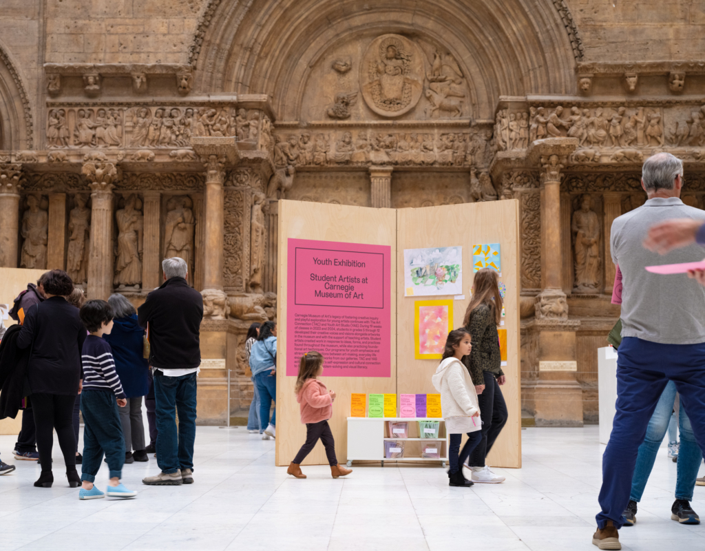 Installation view of Youth Art Exhibition with children and adults walking around the exhibition in the hall of architecture