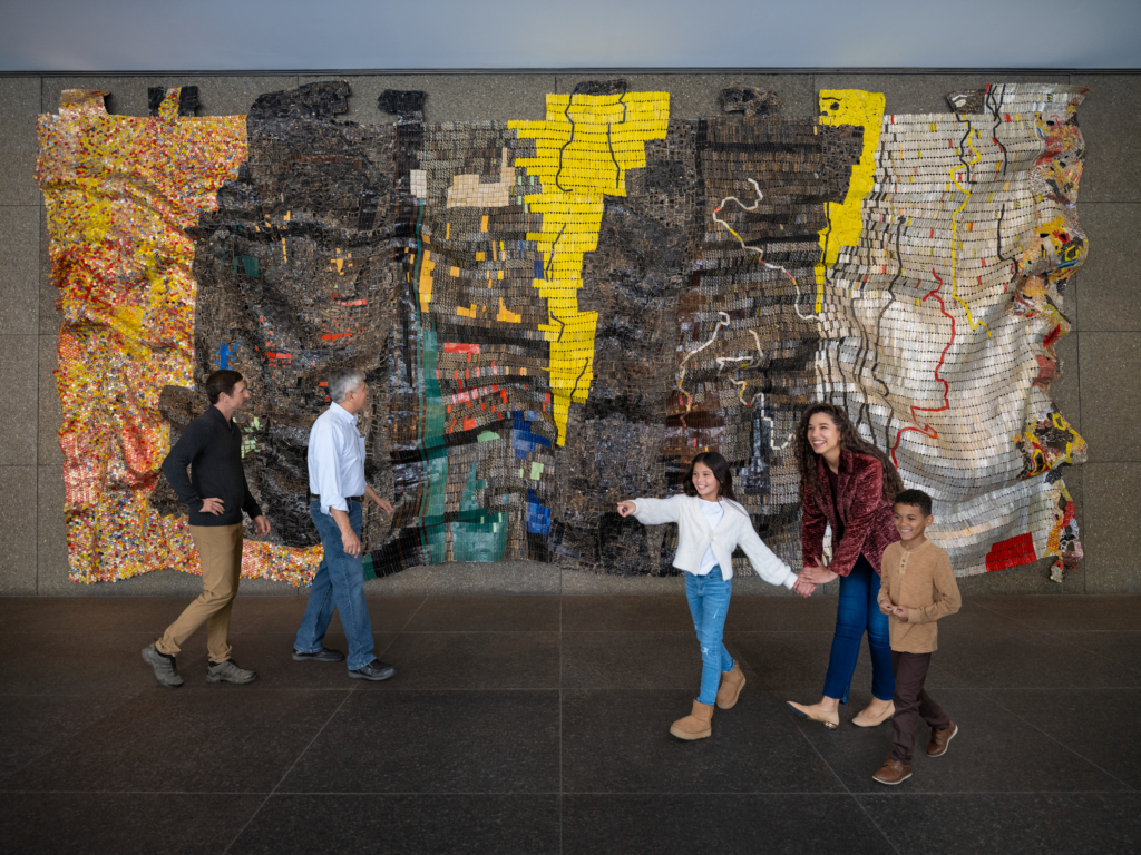 people posing in front of an el anatsui art piece